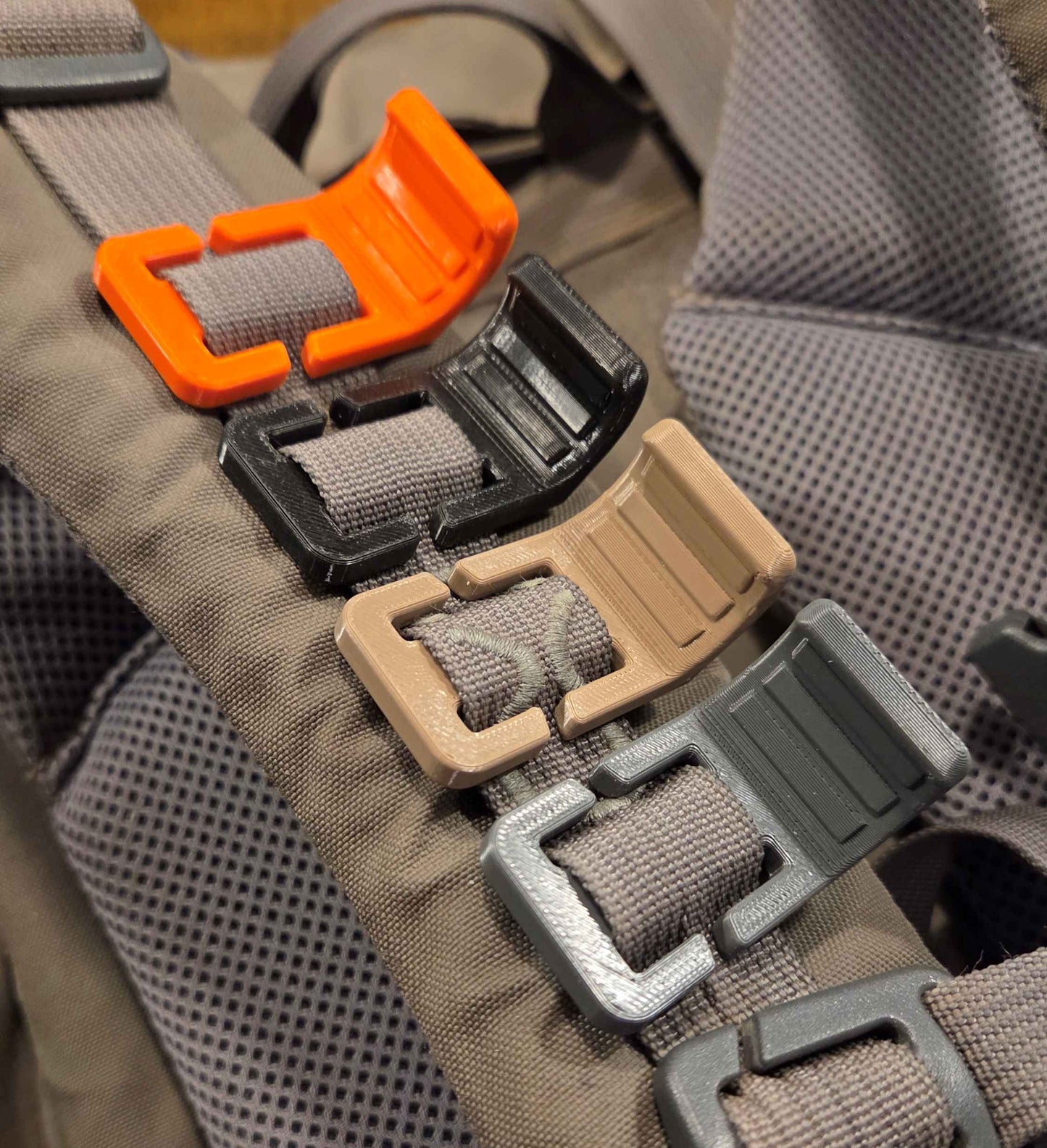 Close-up of an EXO mountain gear backpack with multiple plastic Sling Stops in orange, black, desert, and dark gray attached to the strap.